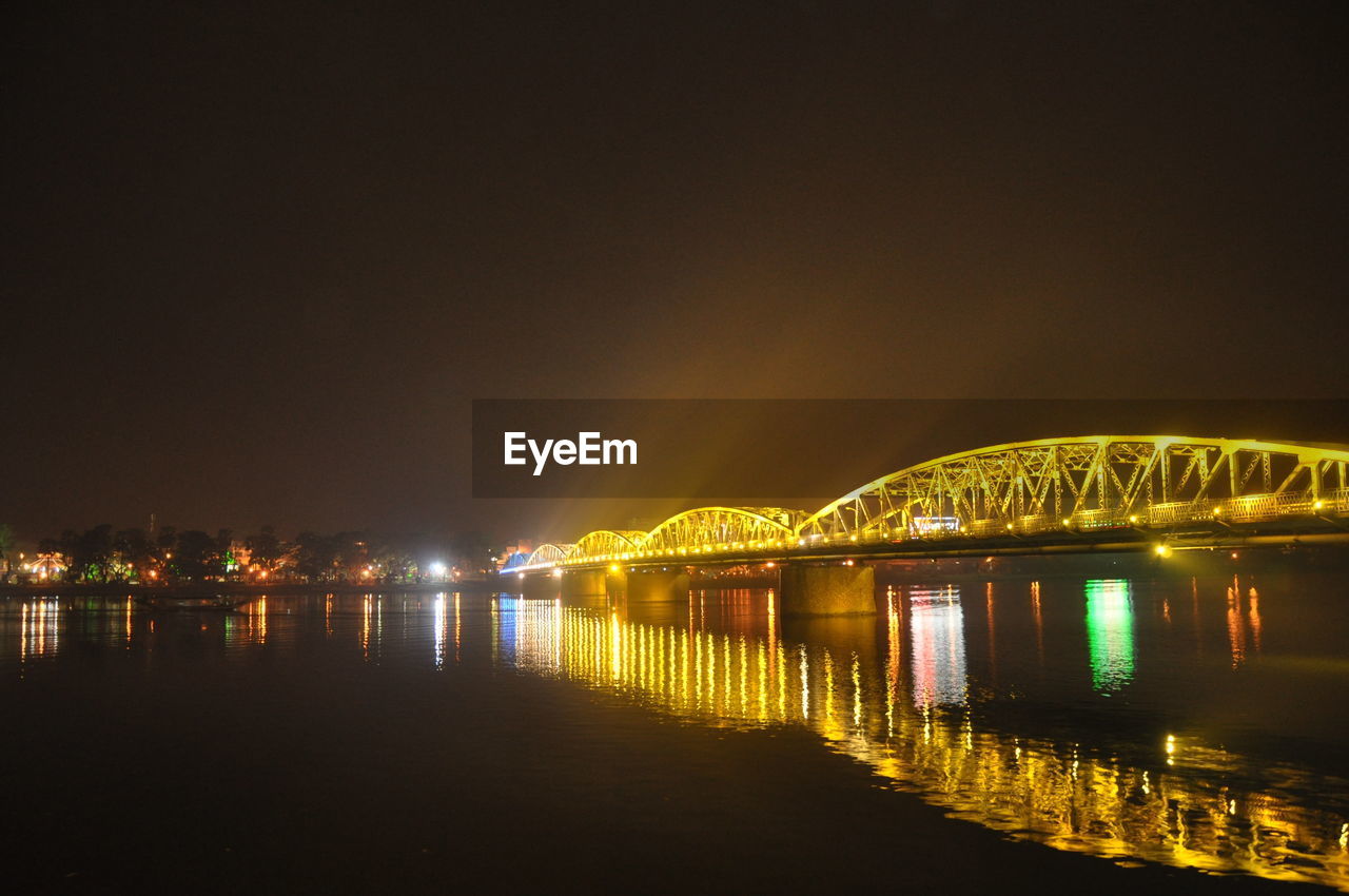 ILLUMINATED BRIDGE OVER RIVER AGAINST SKY AT NIGHT