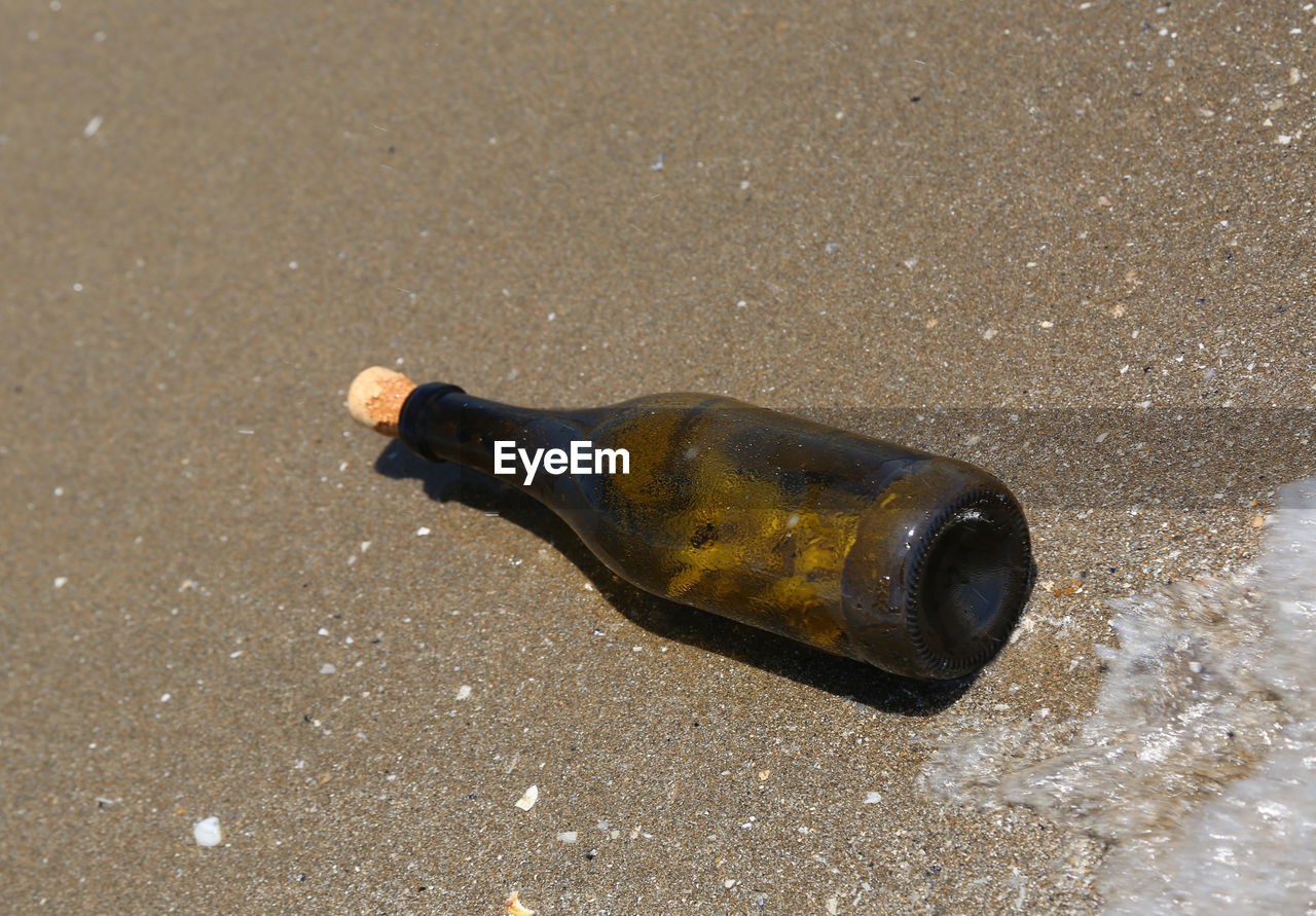 HIGH ANGLE VIEW OF BOTTLE ON SAND
