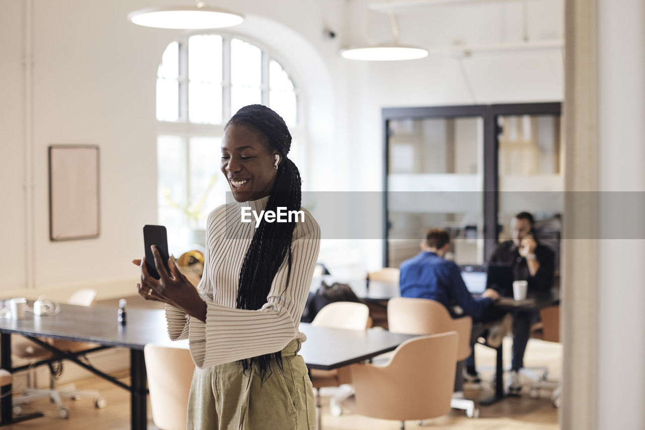 Smiling businesswoman doing video call through mobile phone at coworking office