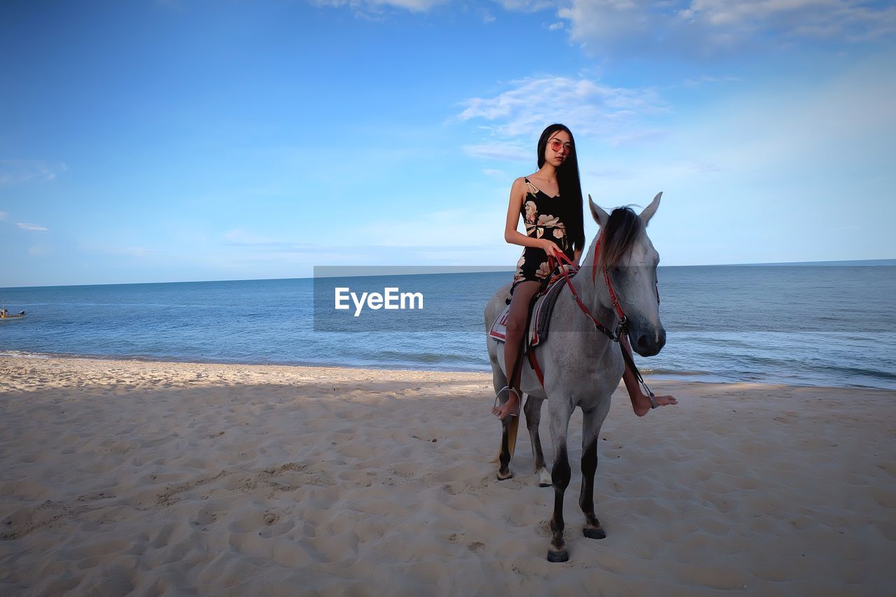 Full length of woman sitting on horse at beach