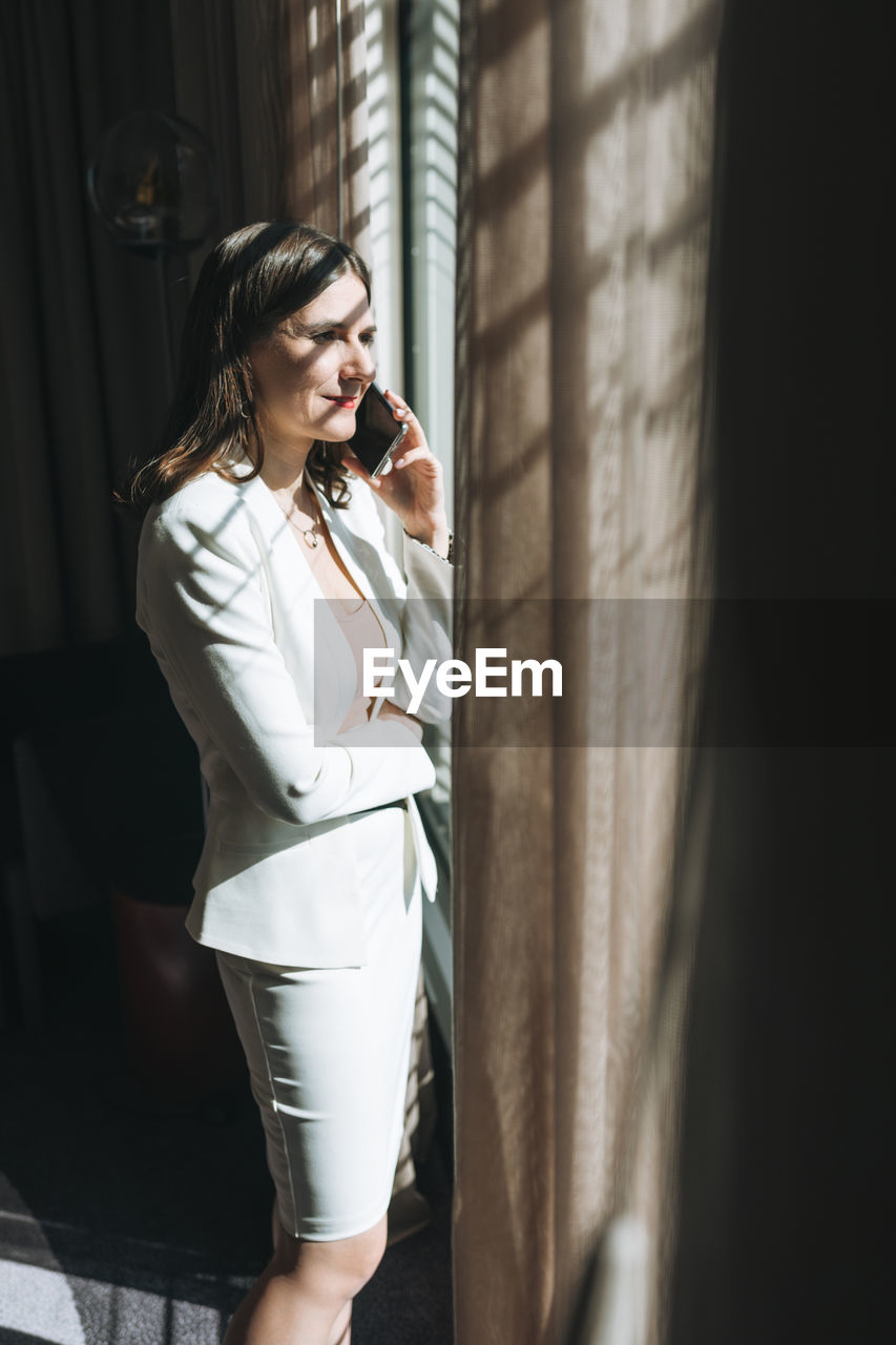 Young brunette woman business lady in white suit with mobile in the hotel room