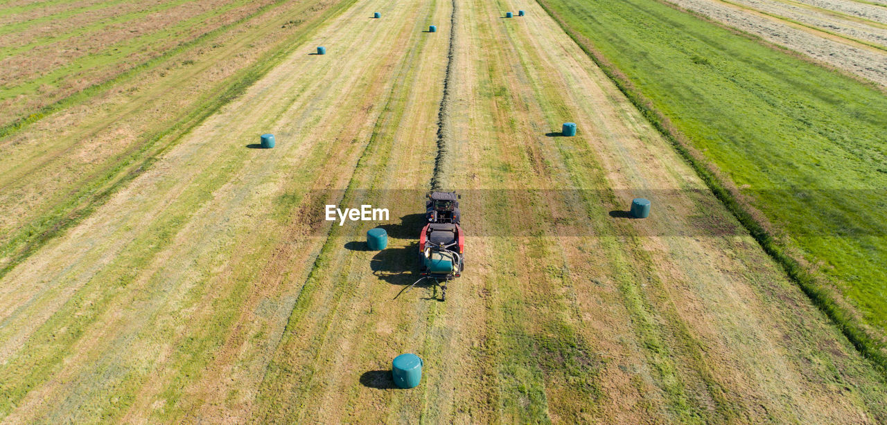 Black tractor with a red straw chamber press during the straw harvest on a mown field