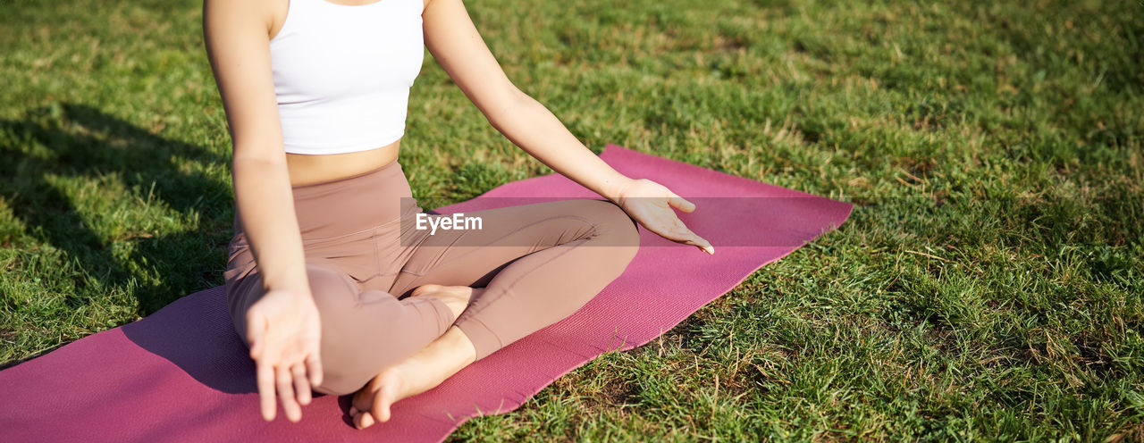 low section of woman meditating on grass