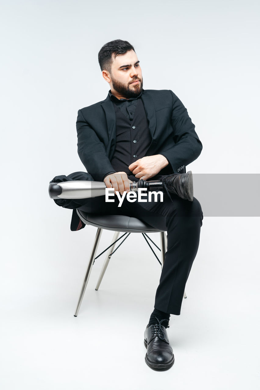 Young man sitting on chair against white background