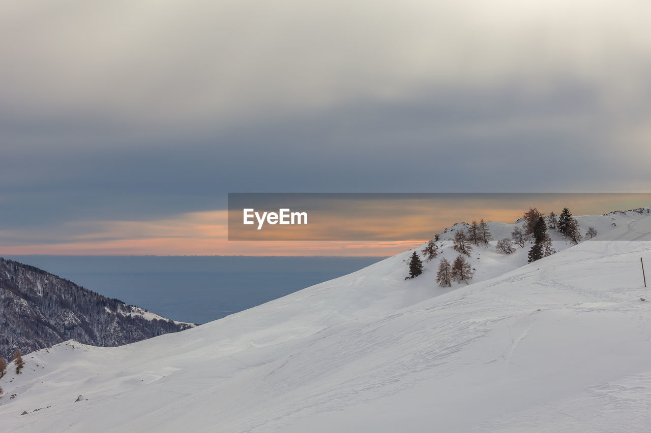 Snow covered landscape against sky during sunset