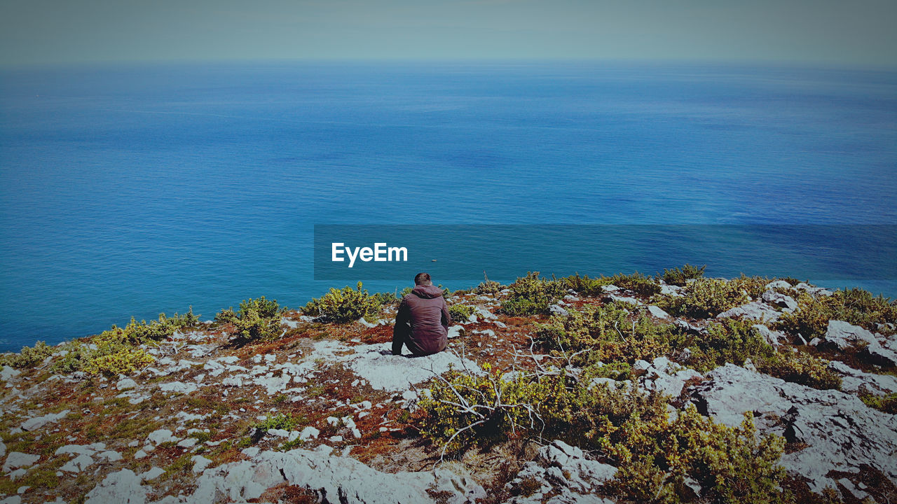 High angle view of man sitting on sea against sky