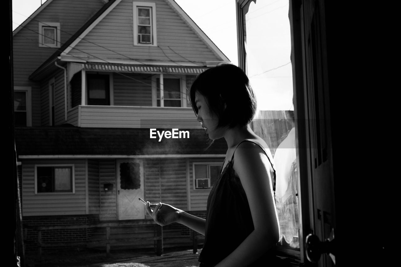 Side view of young woman smoking while standing in balcony