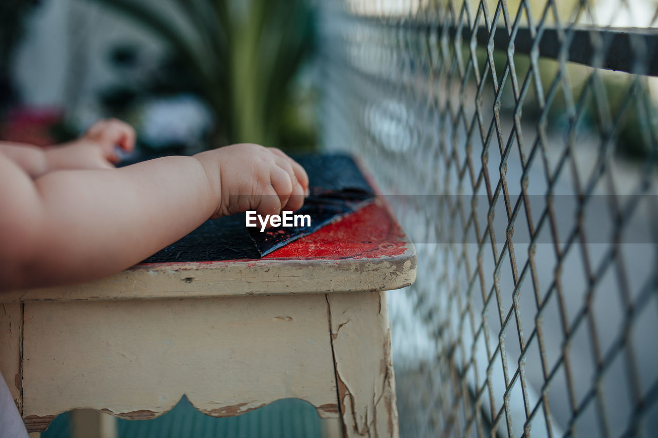 Cropped hands of baby removing plastic from stool by fence