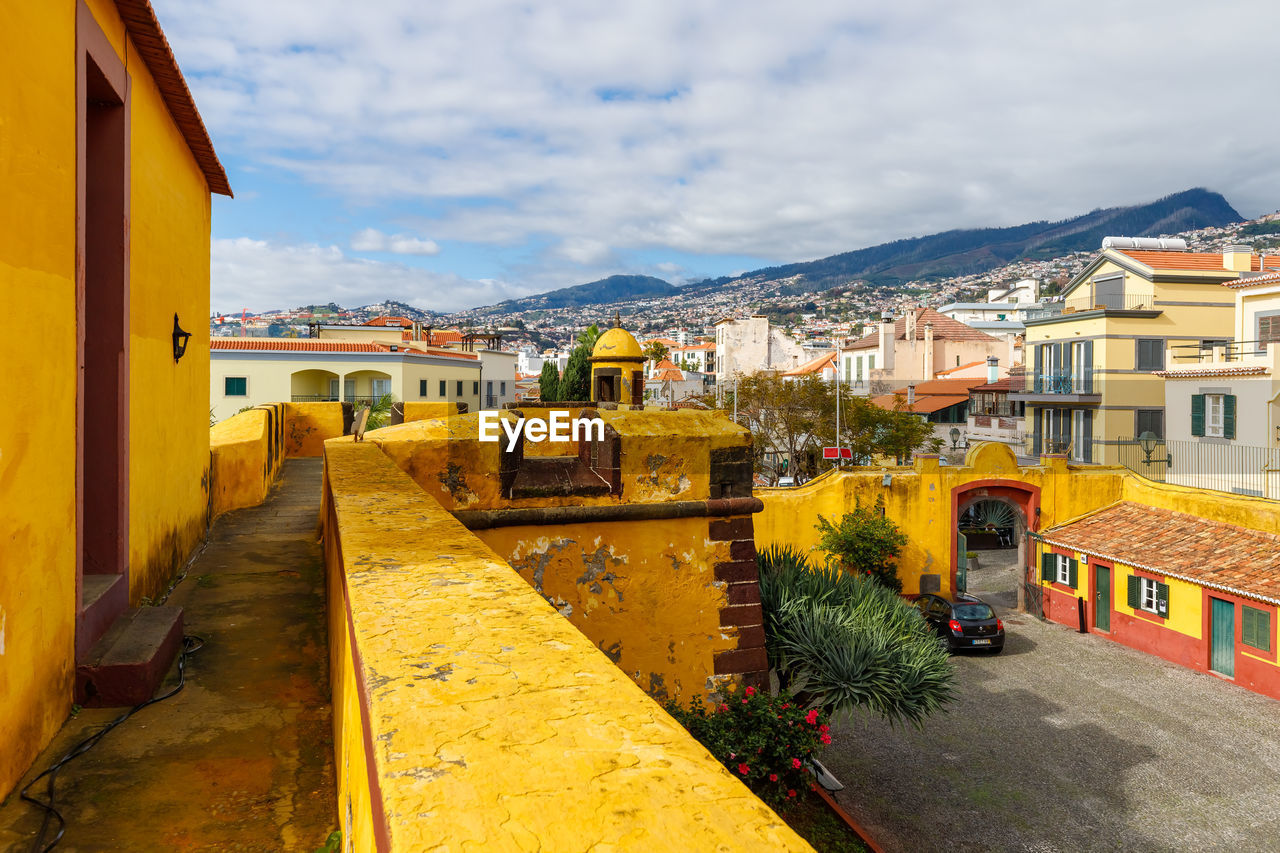 architecture, building exterior, town, built structure, building, city, sky, yellow, nature, residential district, urban area, neighbourhood, vacation, house, cloud, mountain, travel destinations, street, road, cityscape, no people, transport, travel, outdoors, village, transportation, water, day, residential area, city life, plant, city street, landscape, tourism
