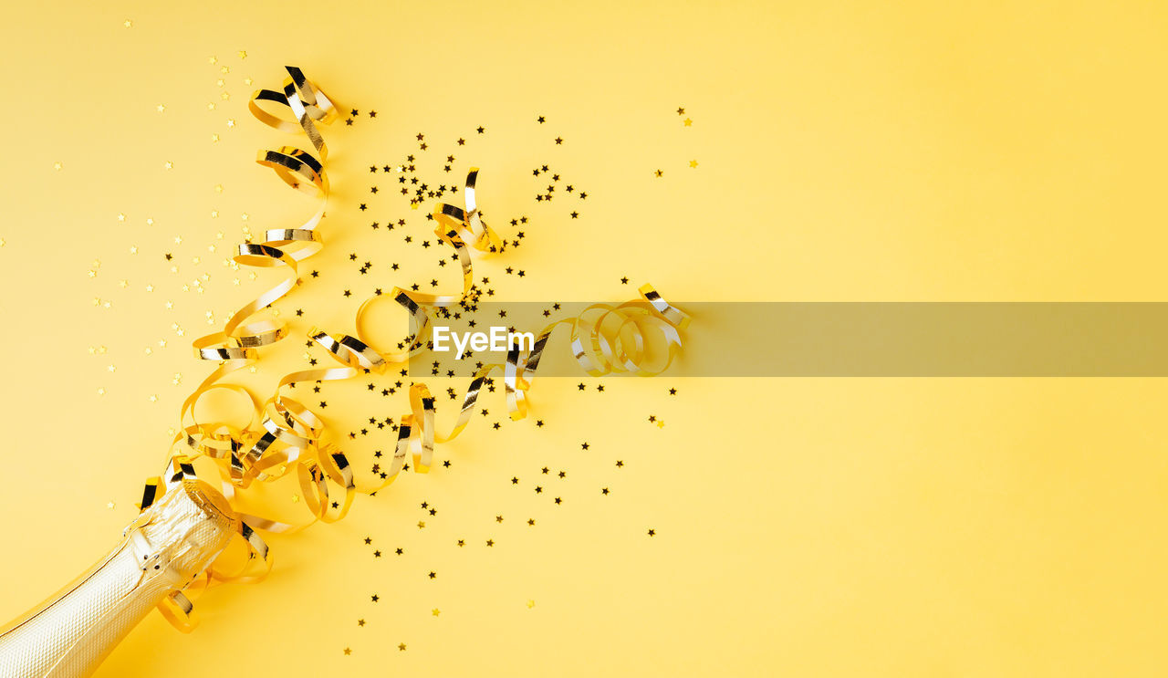 High angle view of champagne with confetti on yellow background