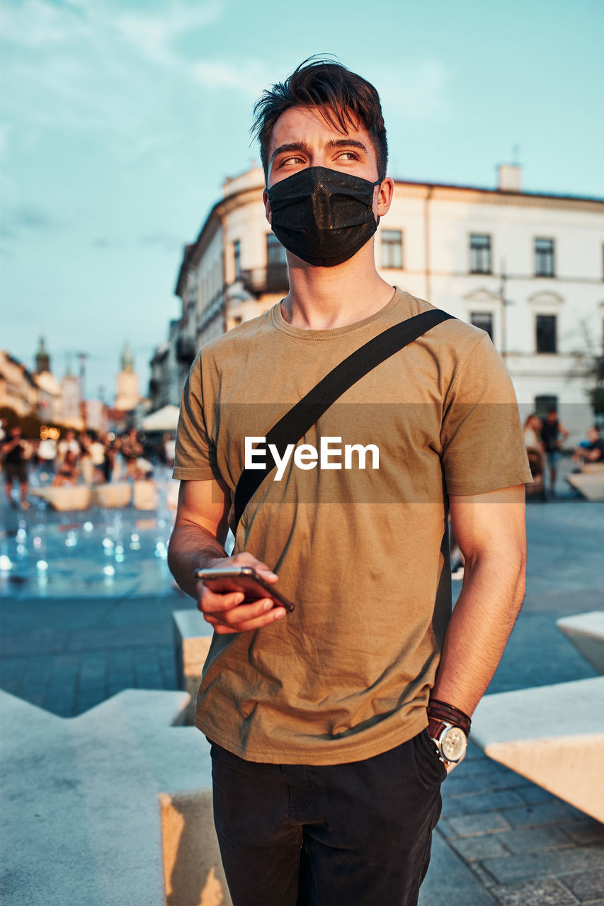 Young man wearing mask looking away while standing outdoors