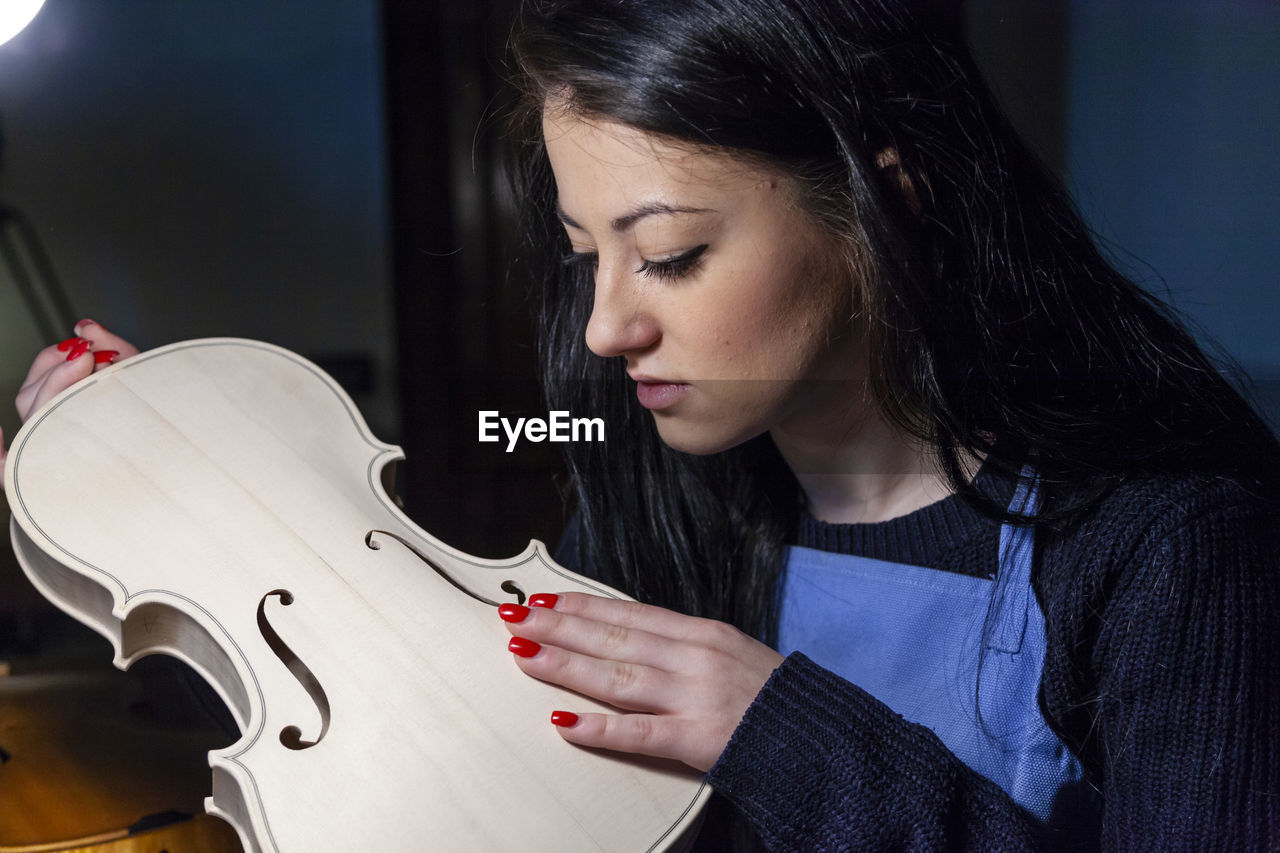 Young woman apprentice violinmaker checking the beauty of her violin