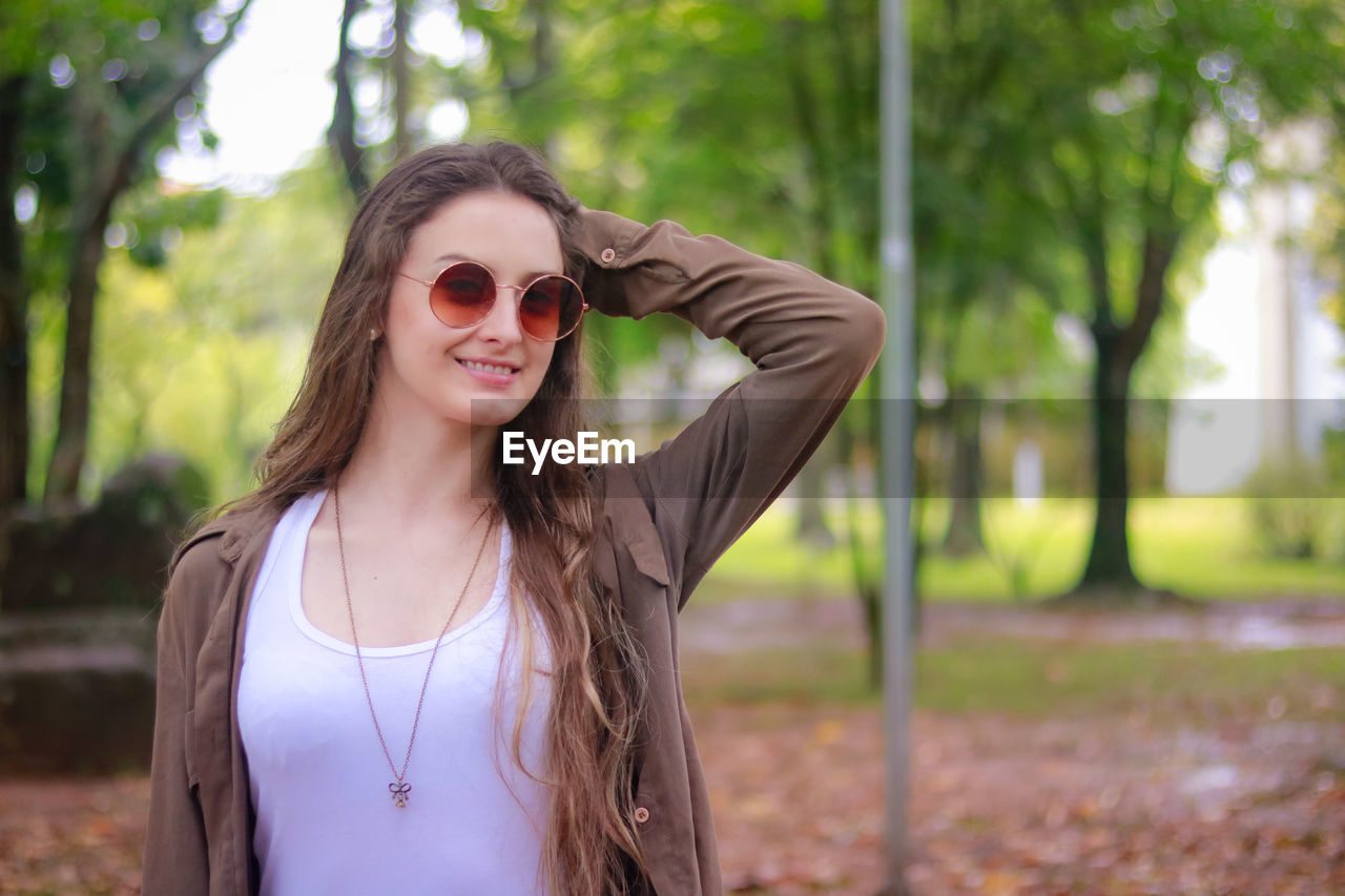 Portrait of smiling beautiful woman wearing sunglasses against trees