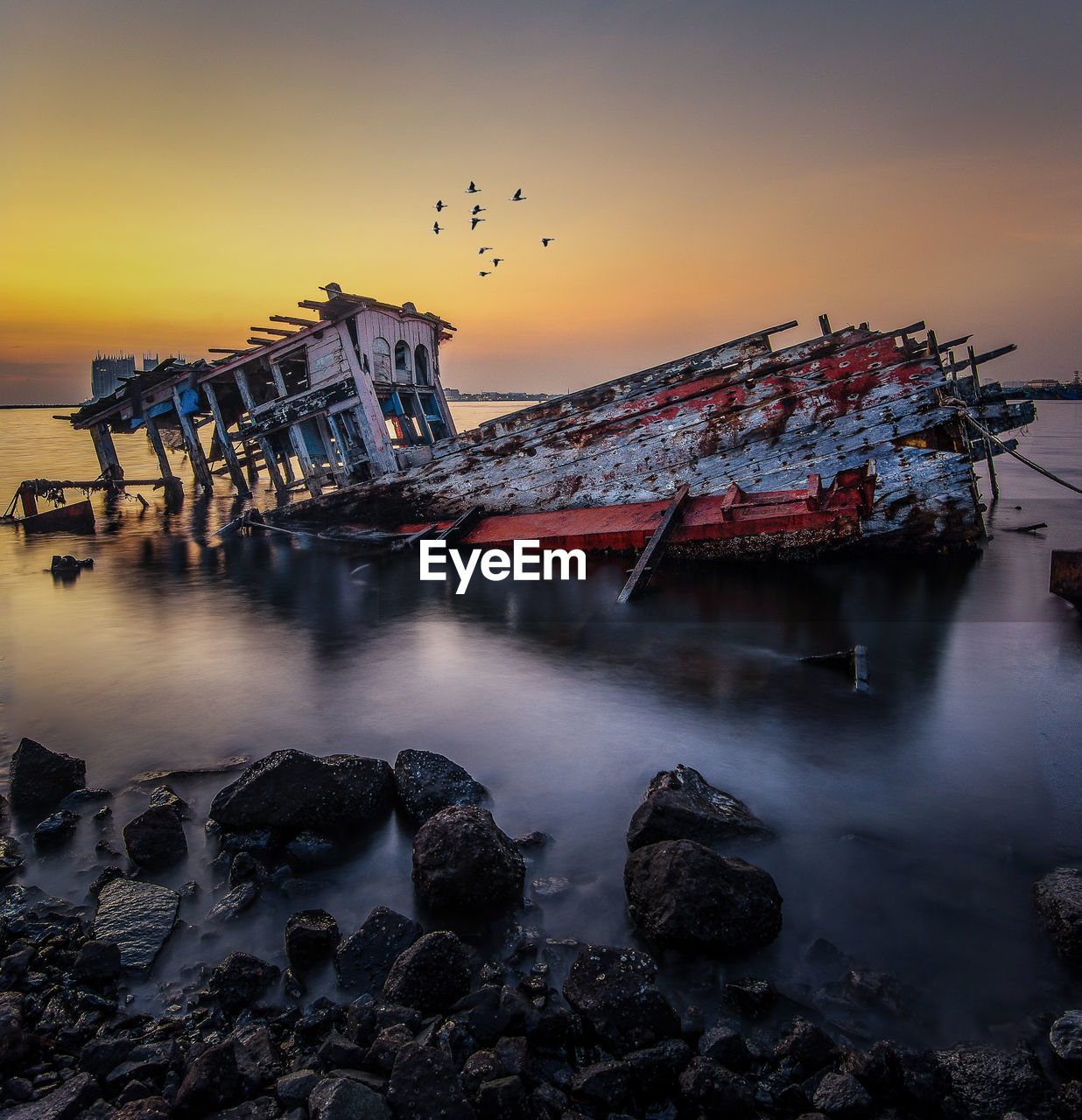 Ship wreck in sea against sky during sunset