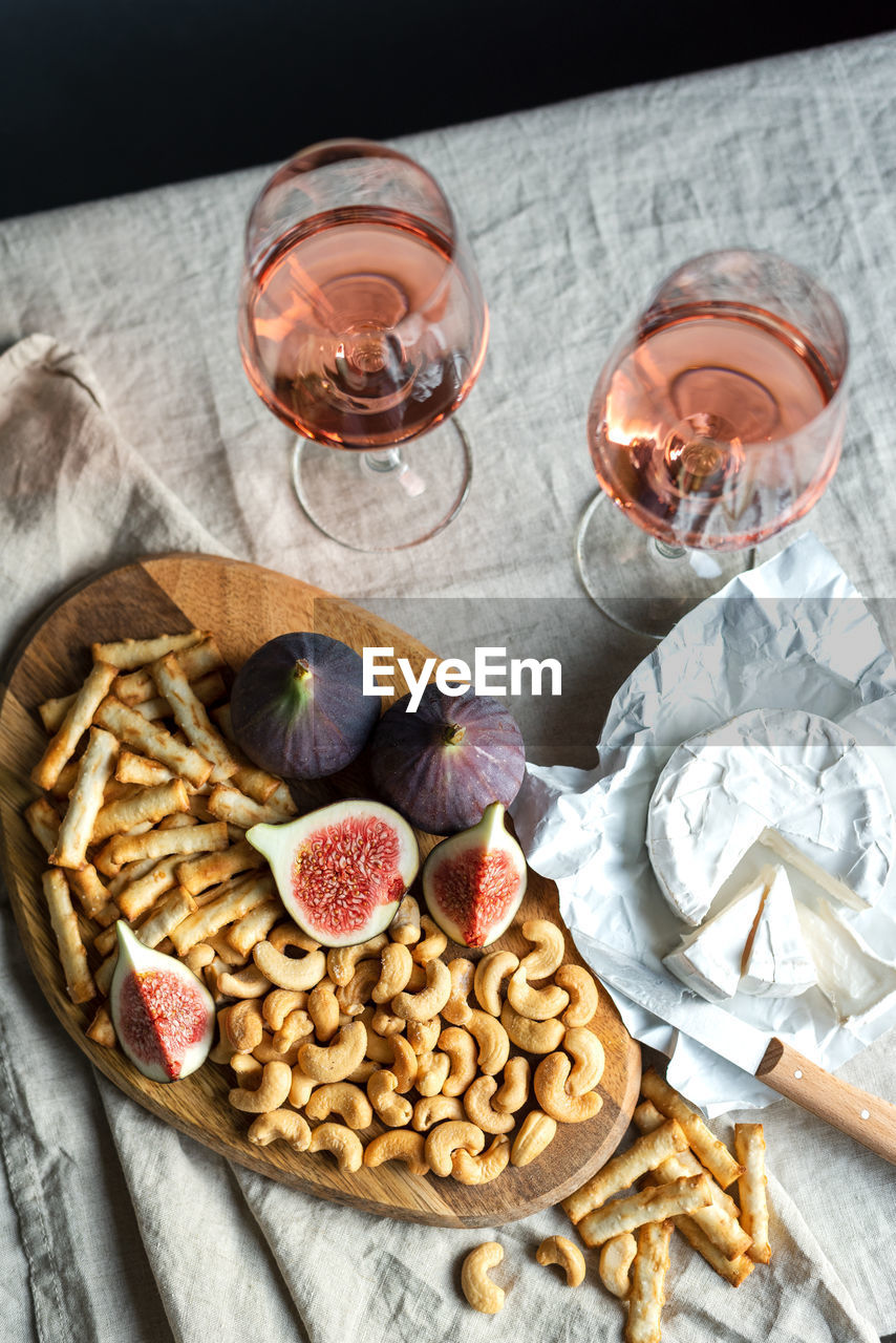 Rose wine with ripe figs, camembert cheese and cashews on a table indoors.