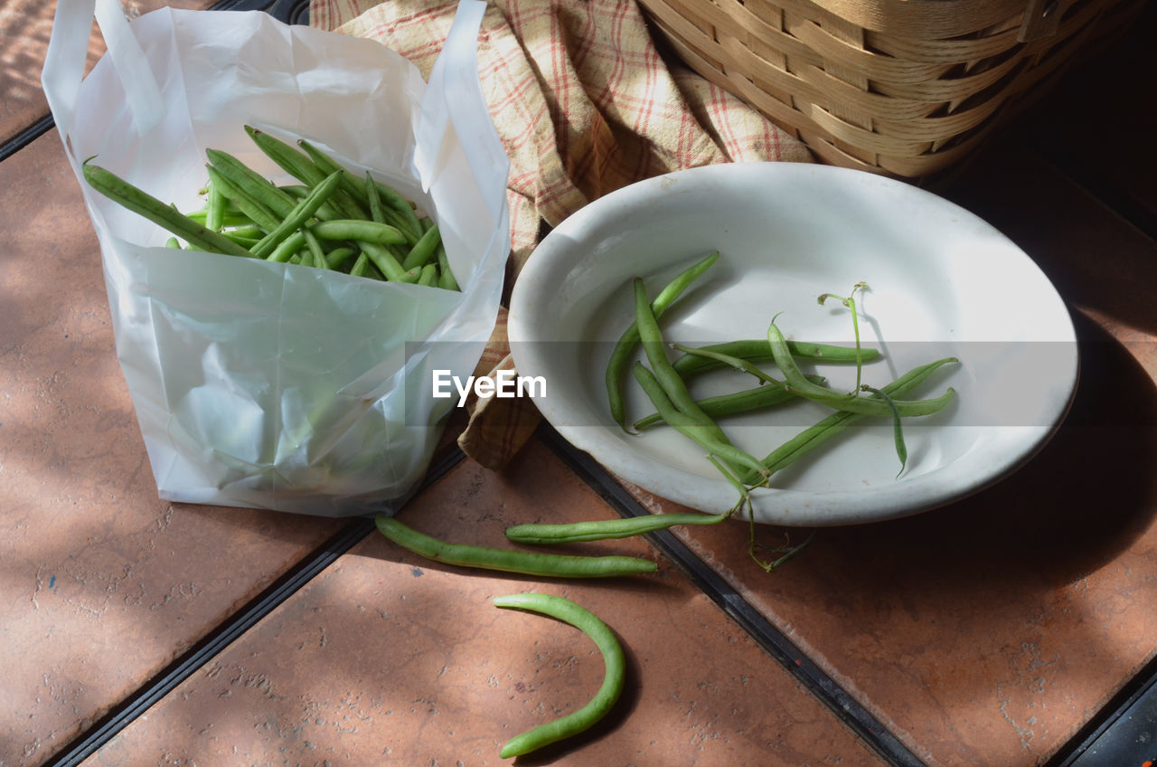 Green beans, white dish with prepared green beans ready for cooking, basket on outdoor table