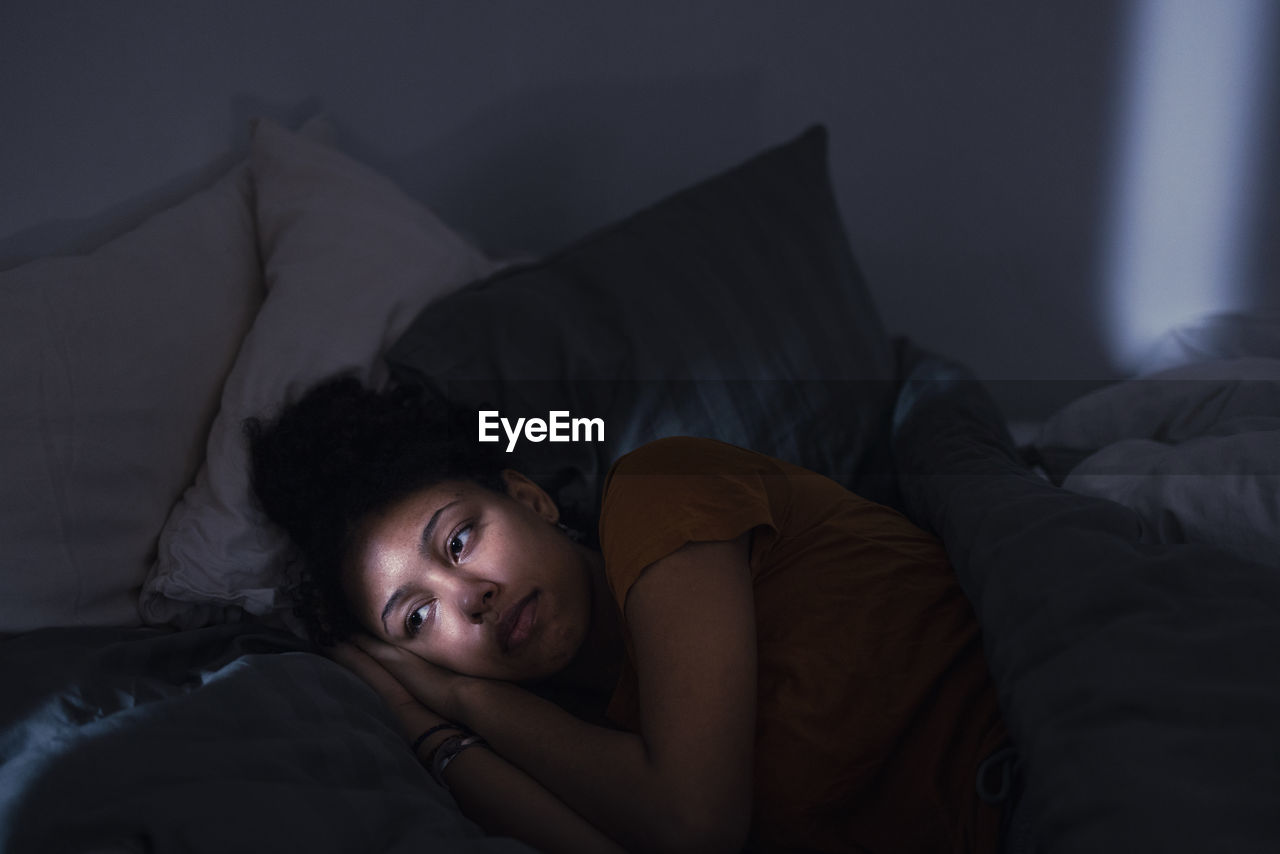 Pensive young woman lying in bed