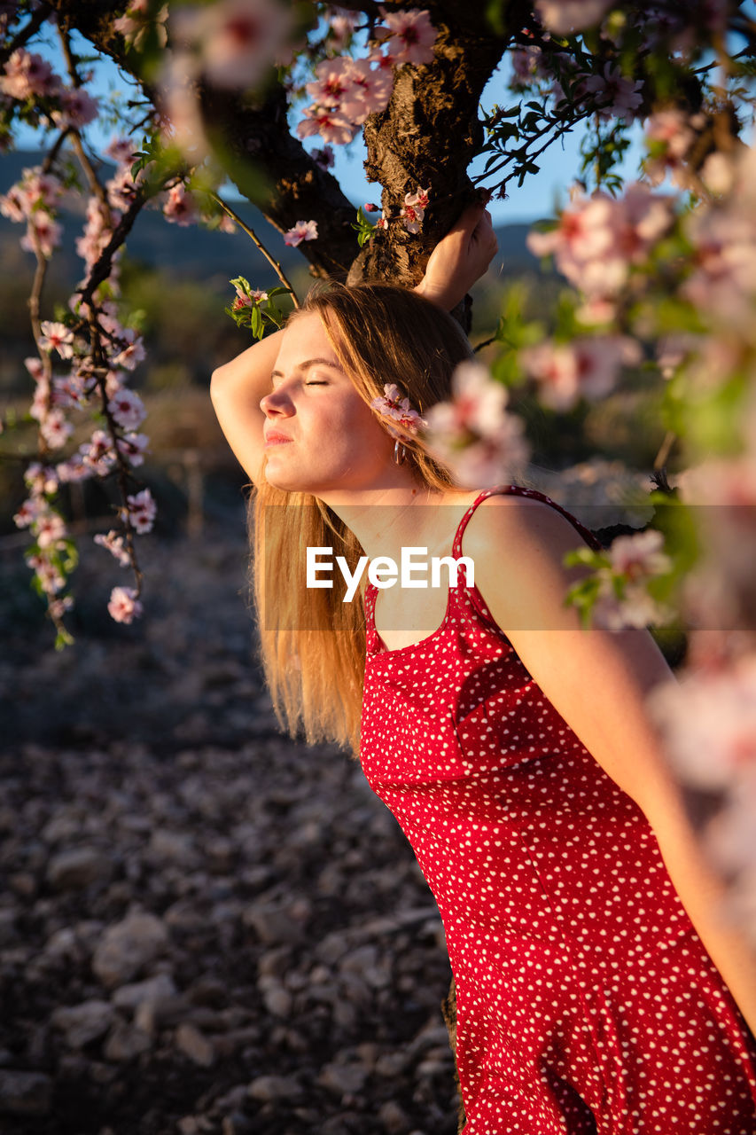 Blond woman with long hair posing under a flowering almond tree