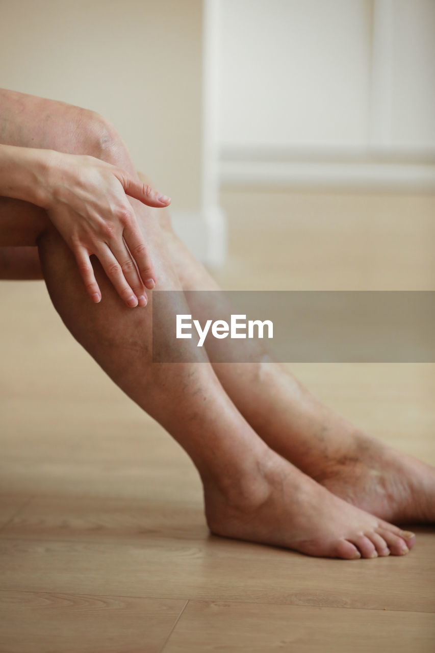 adult, indoors, barefoot, human leg, women, one person, limb, hand, human limb, human foot, flooring, low section, lifestyles, toe, close-up, relaxation, female, wood, arm, hardwood floor, sitting, home interior, skin