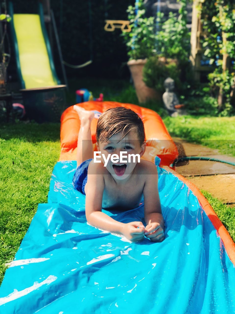 Portrait of boy on water slide at backyard