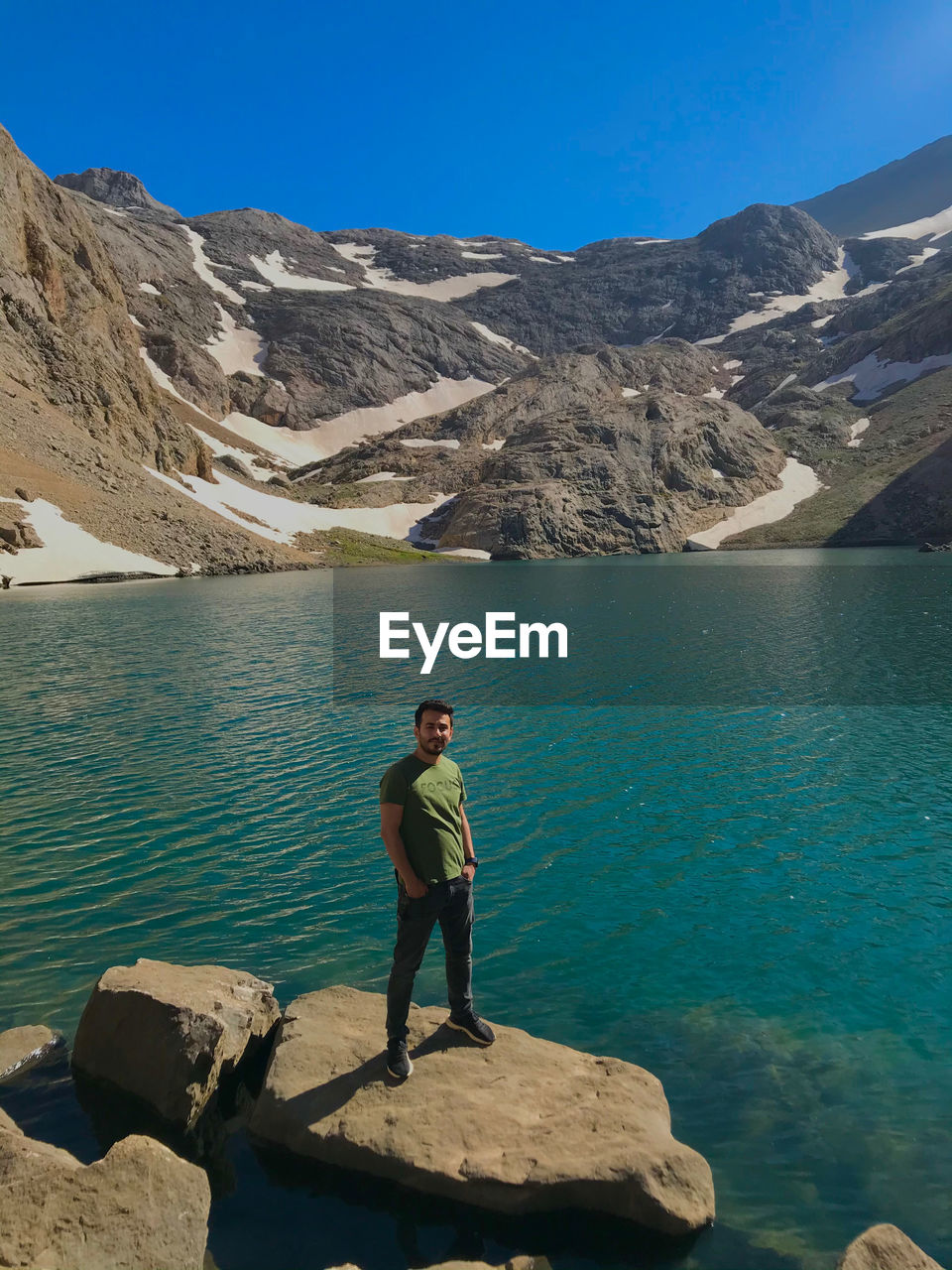 Man standing on rock by lake against sky