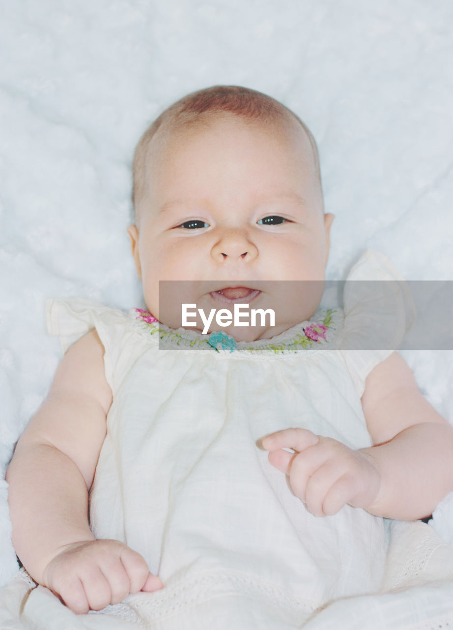 Close-up of cute baby girl showing her tounge laying on white blanket on bed at home