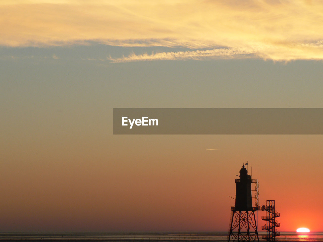 Silhouette lighthouse by sea against orange sky