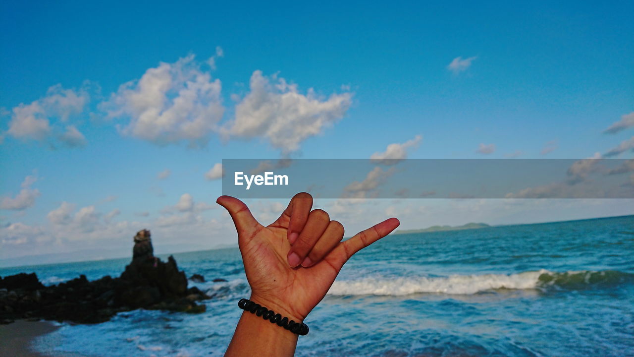 Cropped image of person gesturing by sea against sky