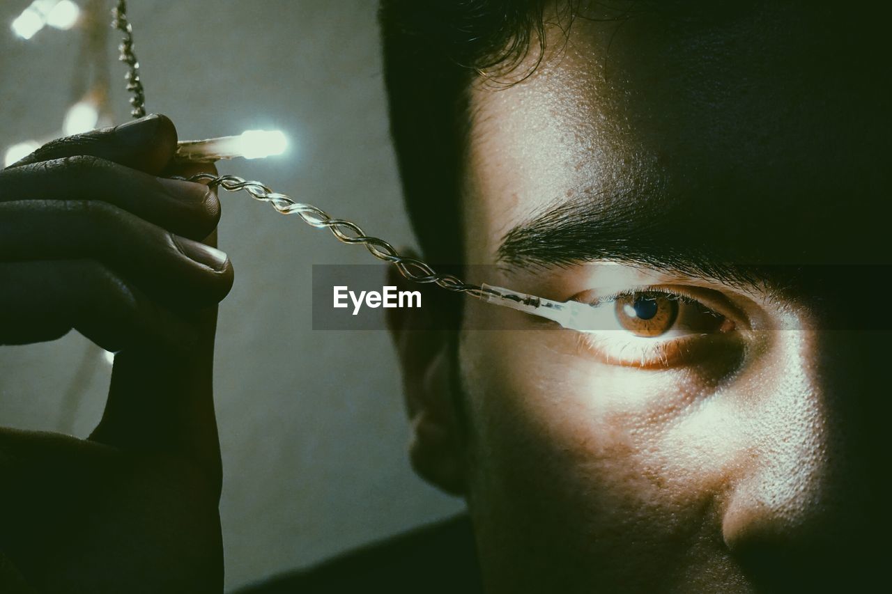 Cropped eye of man with illuminated string light in darkroom