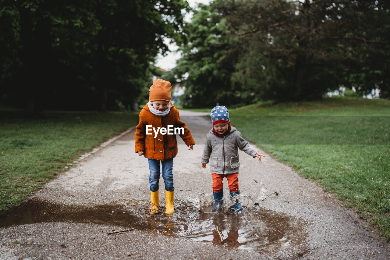 Young boys jumping in the puddles at the park on cloudy day