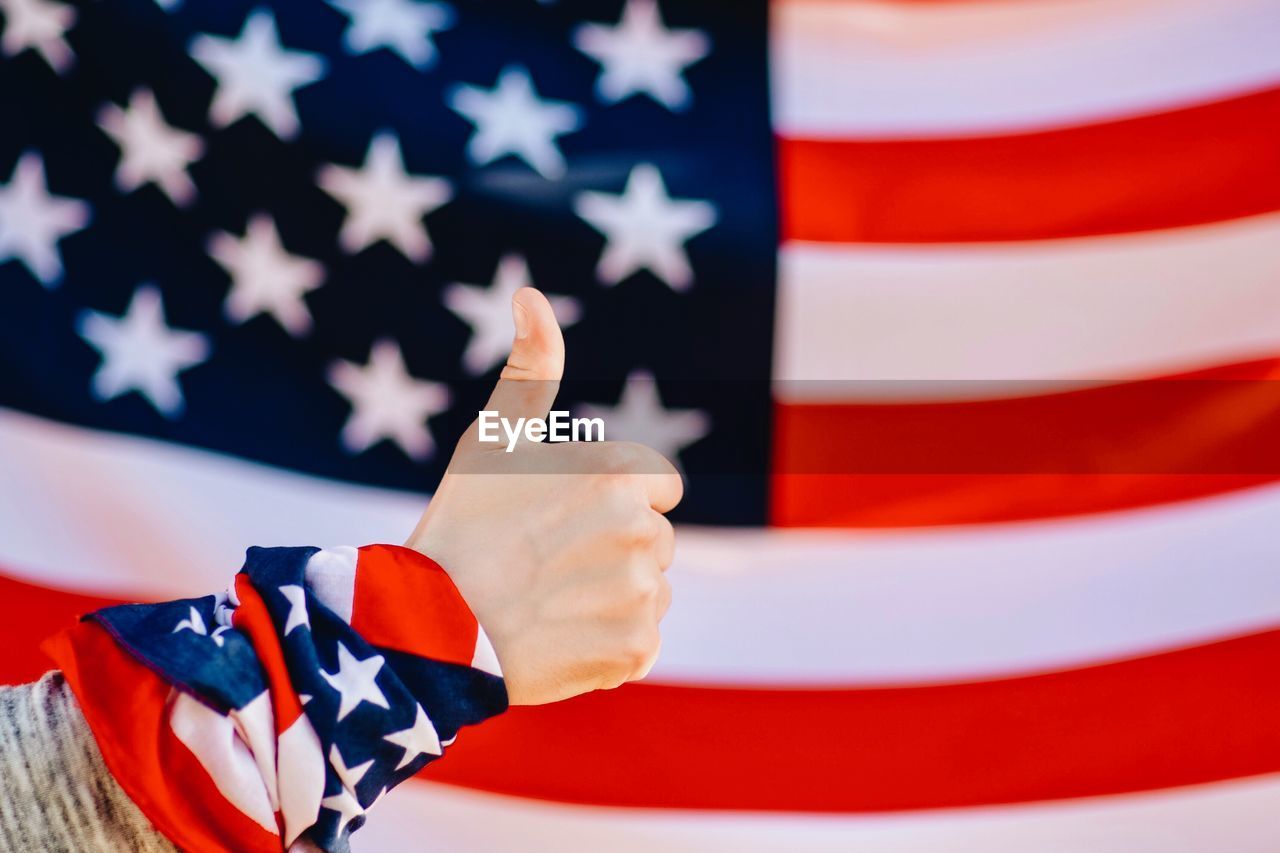 Cropped hand of person showing thumb up against american flag