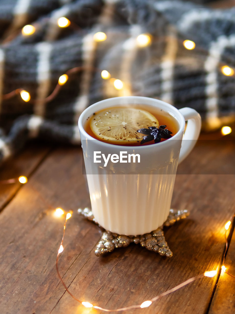 White cup of hot tea with lemon. cozy decorations - grey knitted sweater and light bulbs on wood.