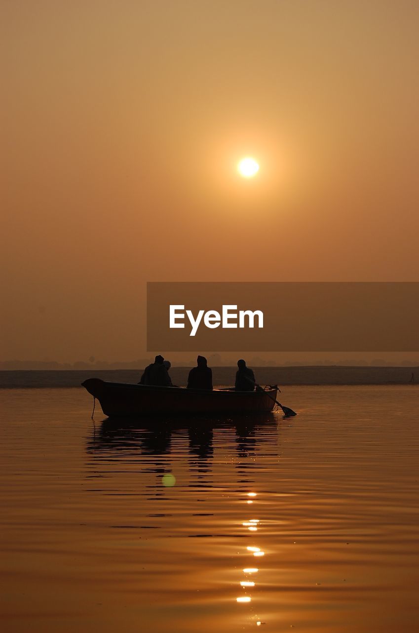 Silhouette people on boat over sea against orange sky