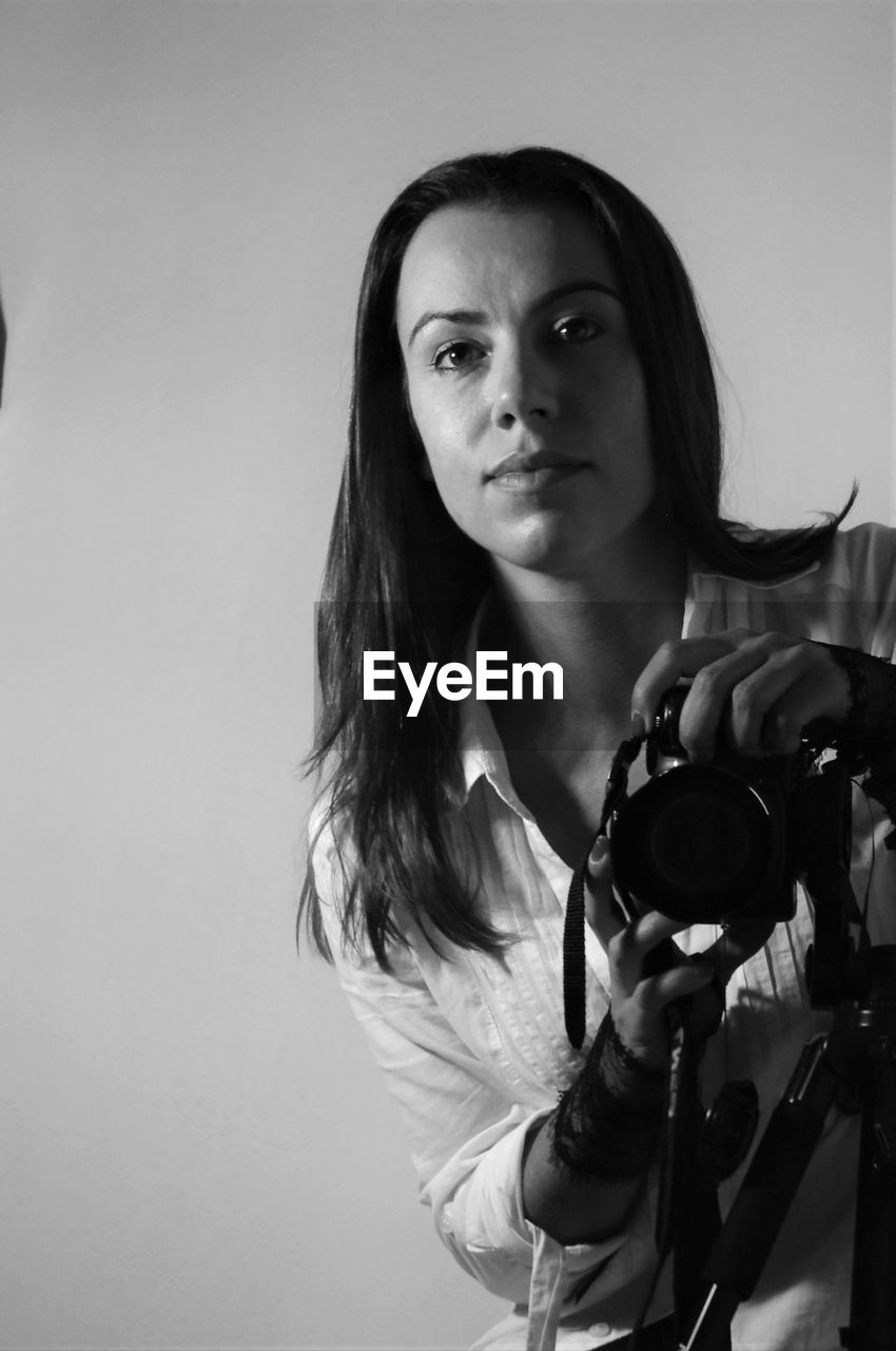 Portrait of photographer holding camera against wall