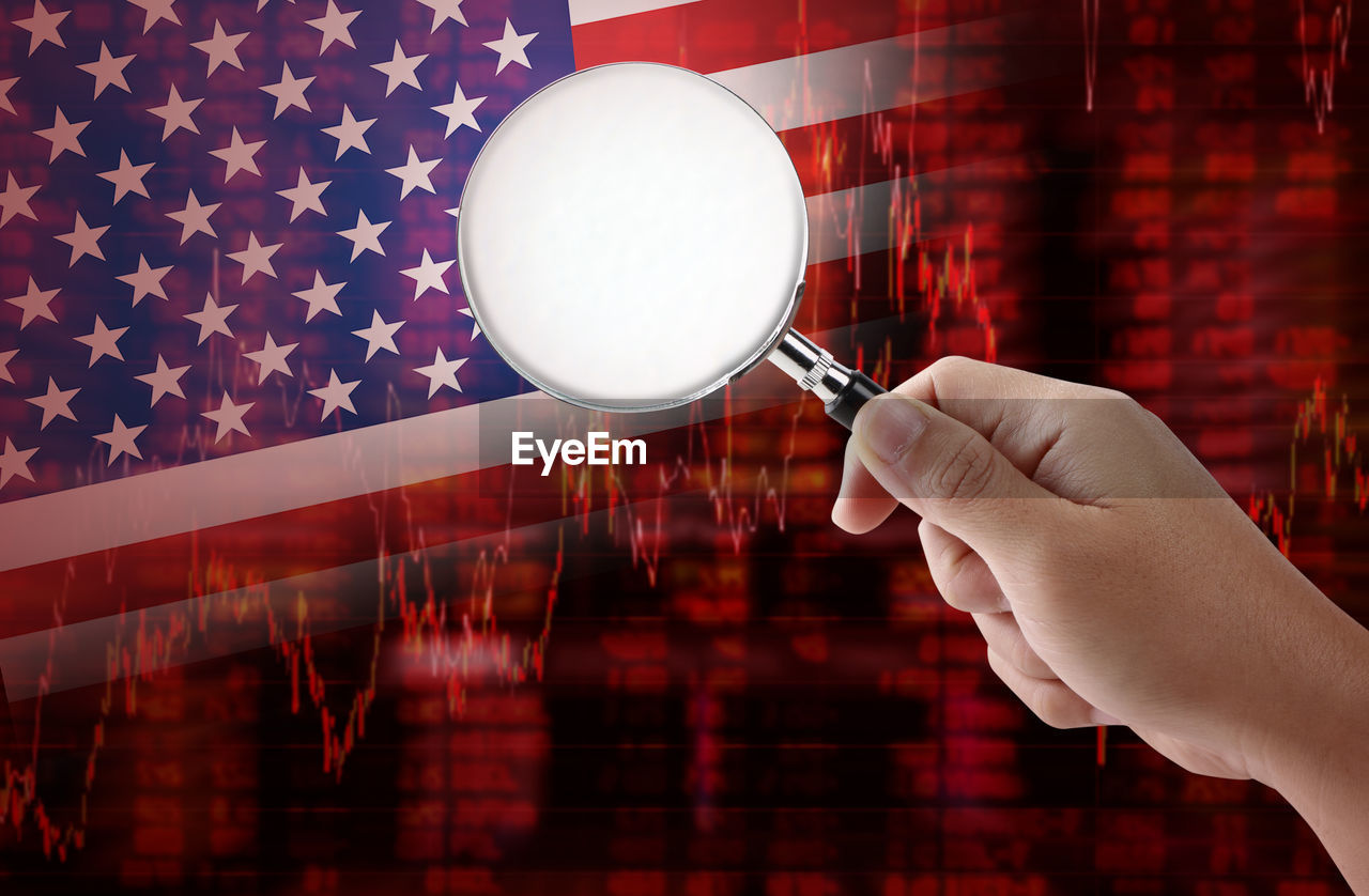 Digital composite image of cropped hand holding magnifying glass against american flag