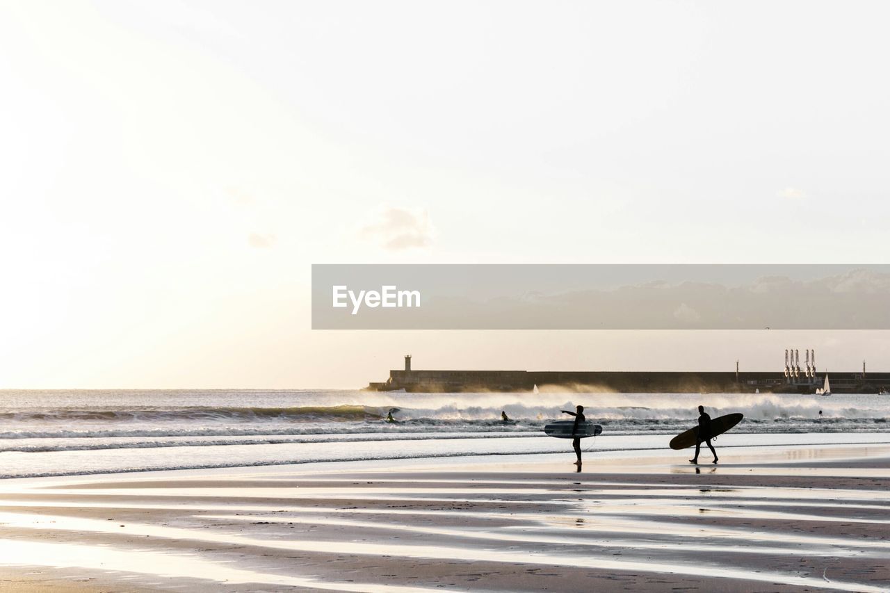 Silhouette people with surfboard at beach against sky