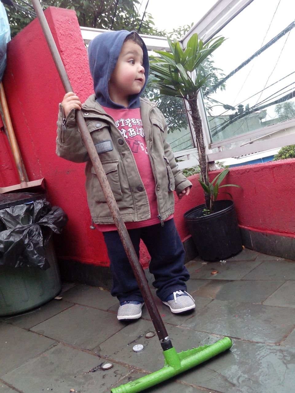 Curious boy holding broken mop on patio