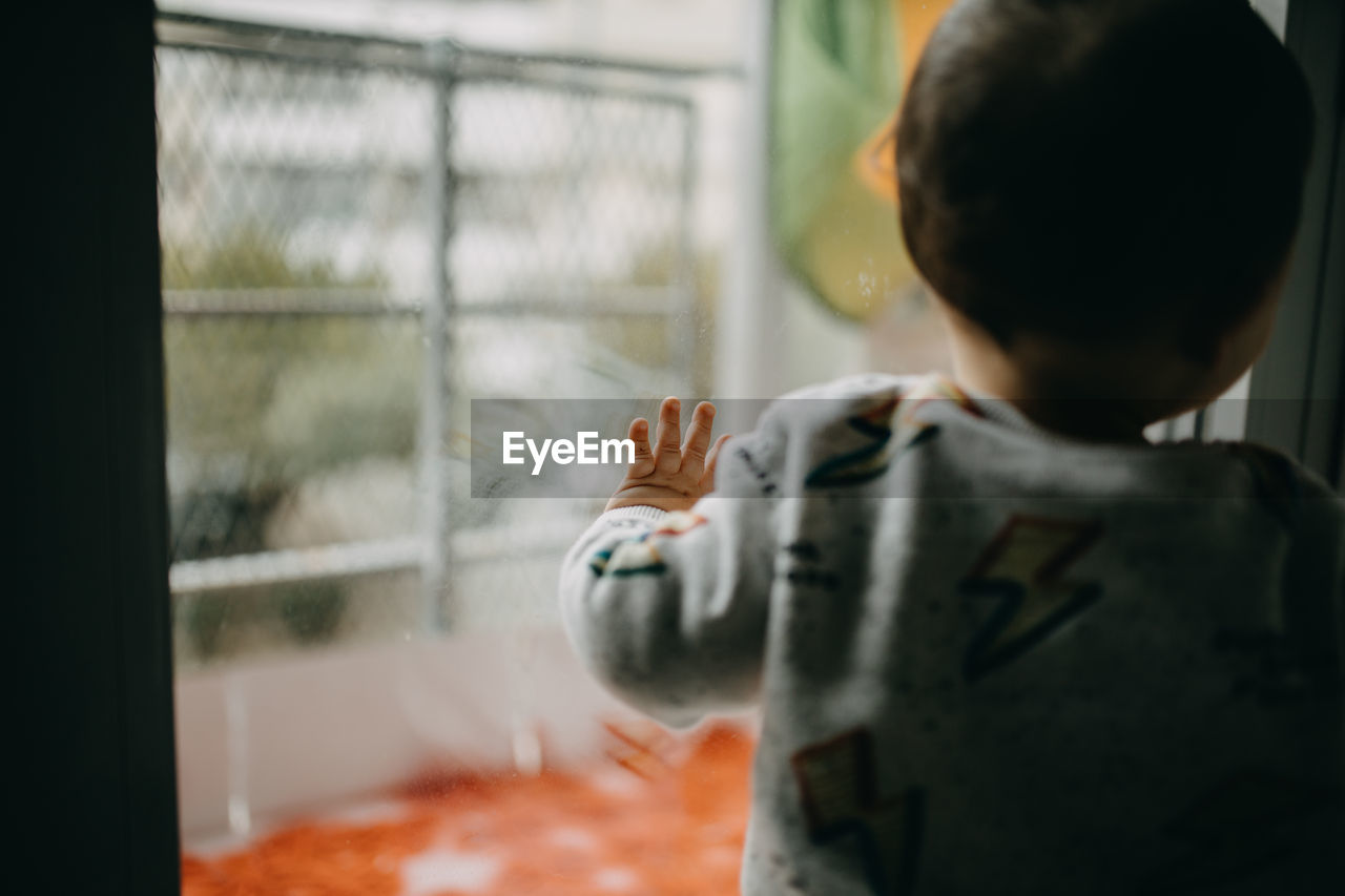 Rear view of boy standing by glass window