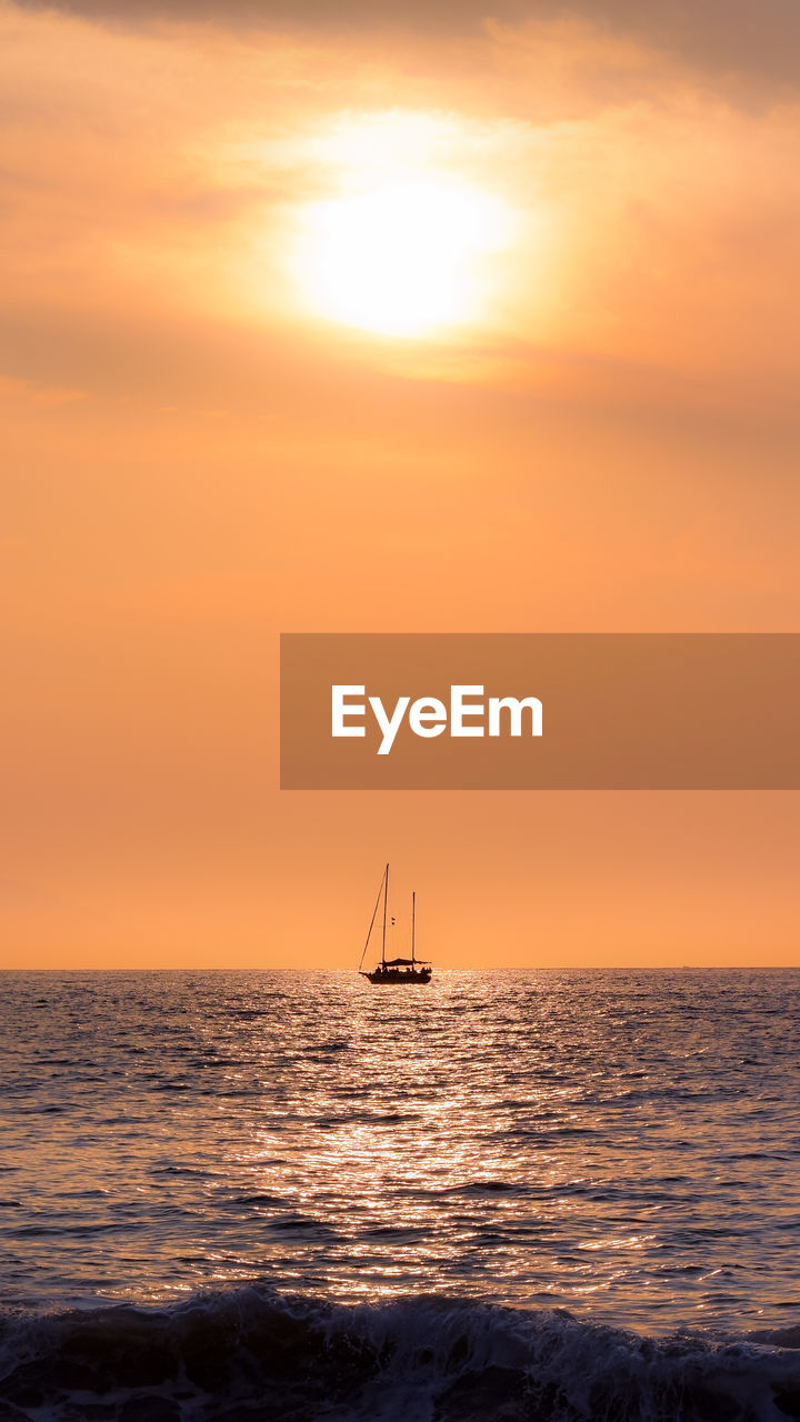 Silhouette sailboat in sea against orange sky