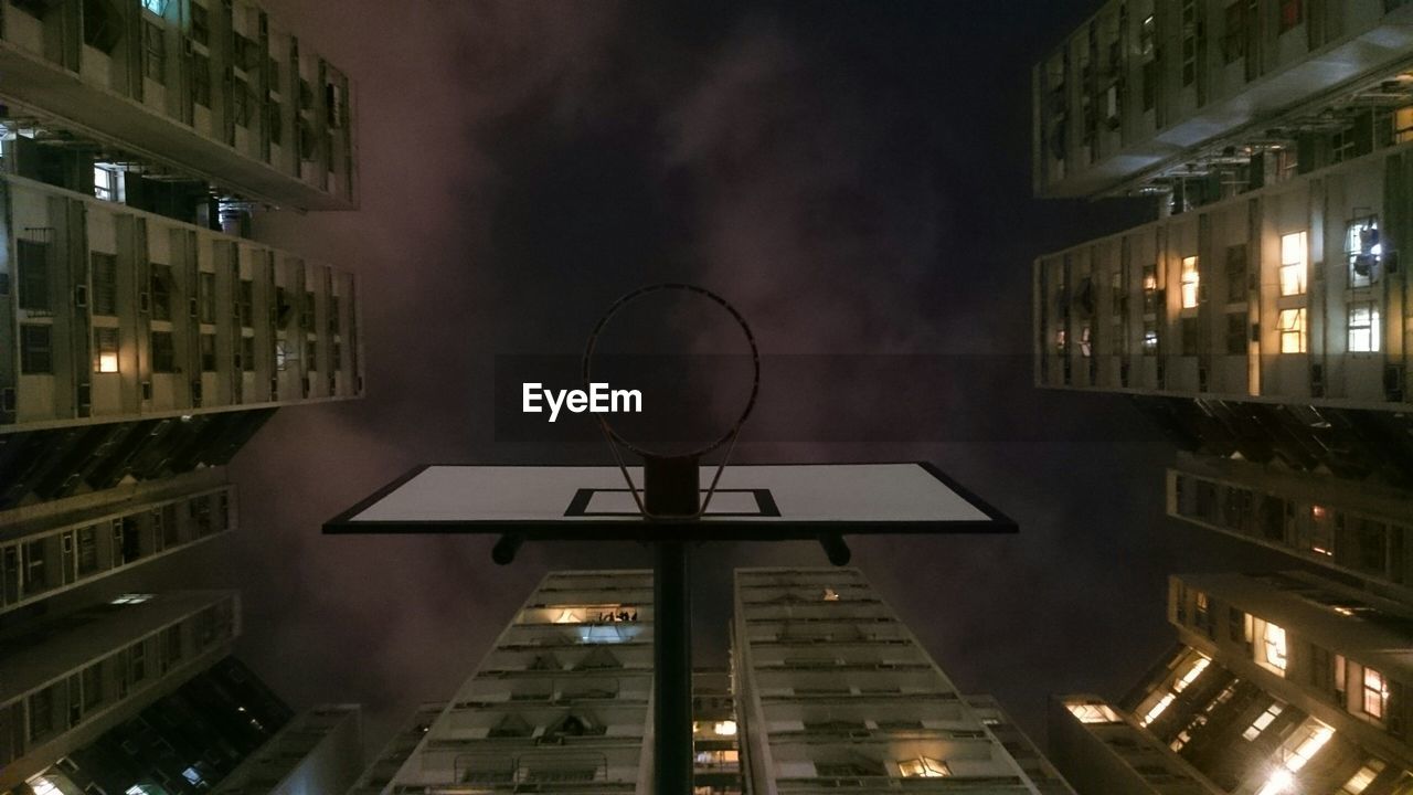 Directly below shot of basketball hoop amidst buildings against sky at night