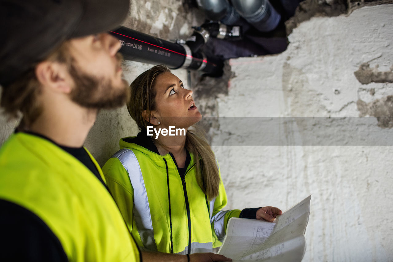 Concentrated male and female plumbers looking up while reading document at basement