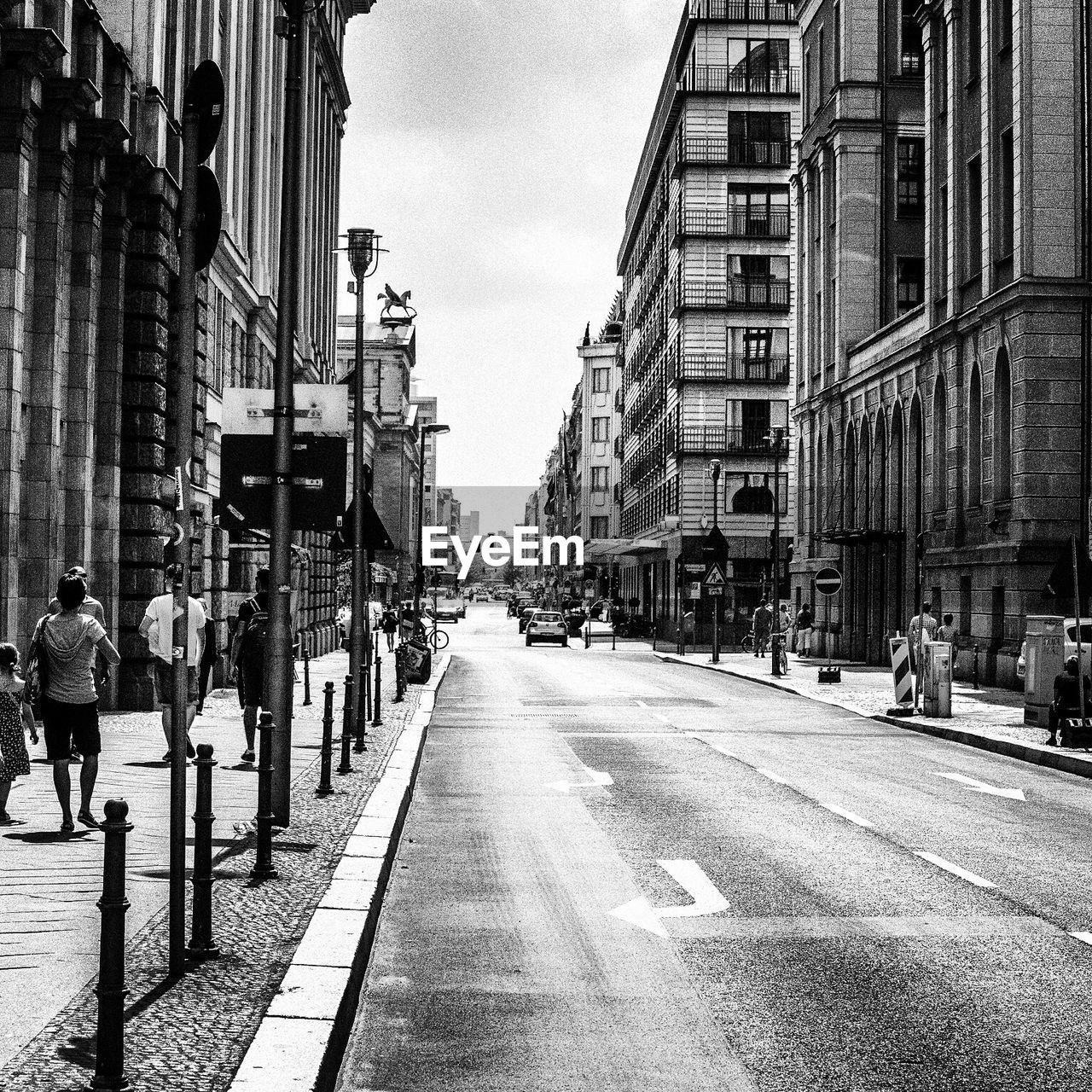 People walking on sidewalk by city street between buildings