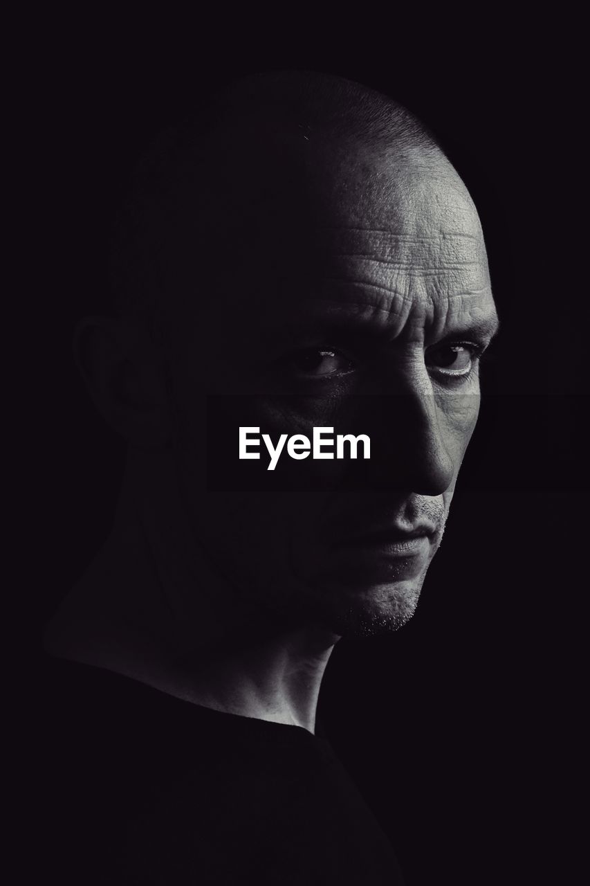 Close-up portrait of serious man against black background