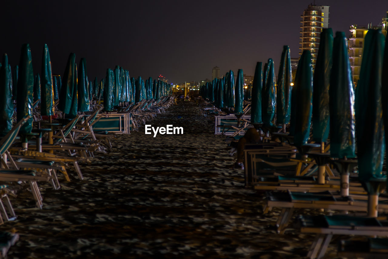 Row of deck chairs and closed parasol at beach against sky