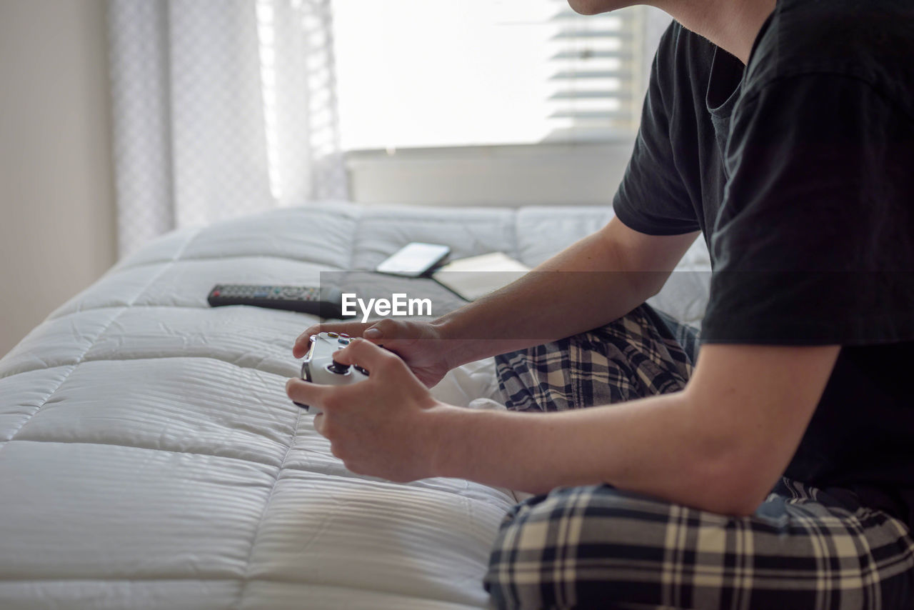 Low section of man playing video game on bed at home