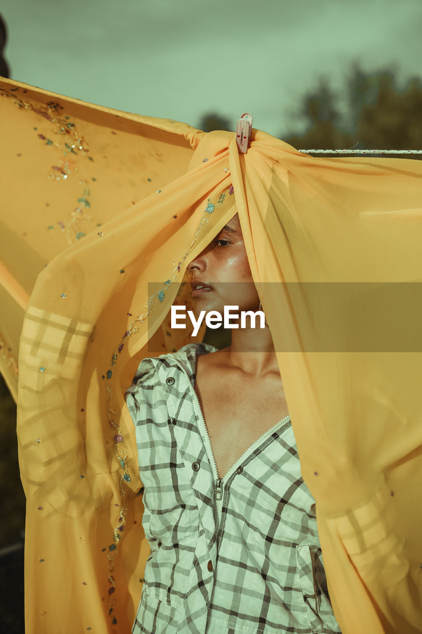 MIDSECTION OF WOMAN HOLDING YELLOW UMBRELLA AGAINST SKY