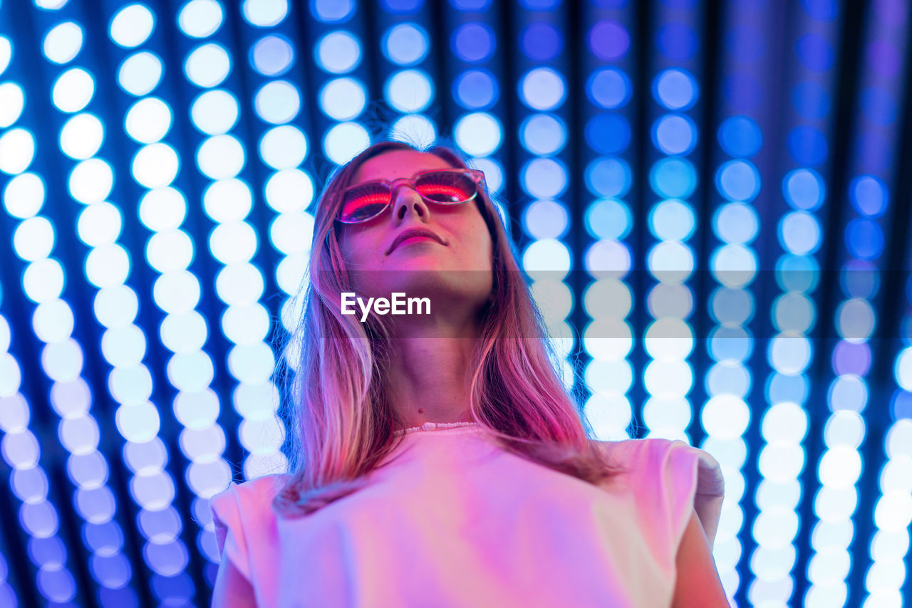 Low angle view of woman wearing sunglasses standing against illuminated ceiling