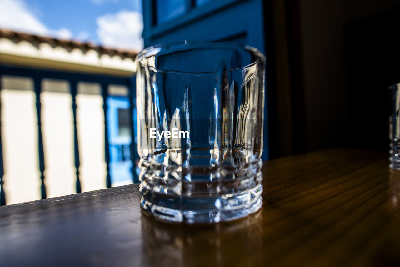 glass, drinking glass, table, food and drink, household equipment, drink, refreshment, no people, water, indoors, wood, close-up, blue, reflection, focus on foreground, selective focus, alcoholic beverage, nature, transparent, highball glass, drinking water, bar, old fashioned glass, freshness