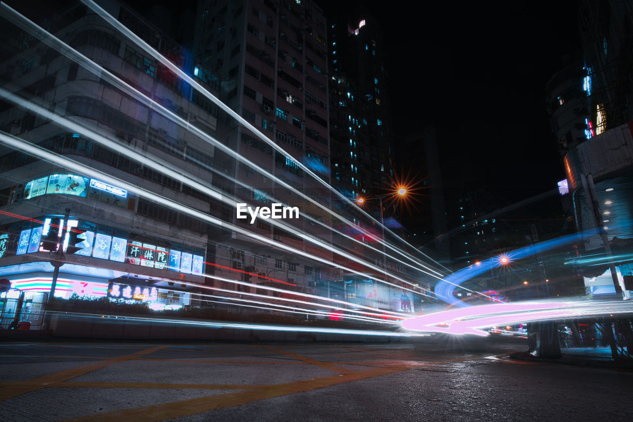 LIGHT TRAILS ON CITY STREET AGAINST ILLUMINATED BUILDINGS AT NIGHT