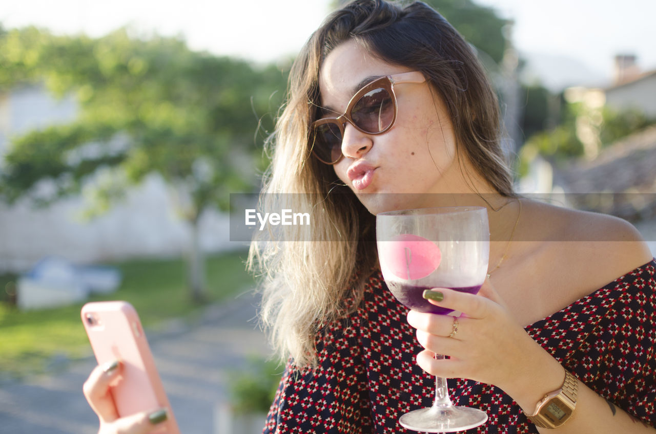 Young woman having drink while using phone outdoors